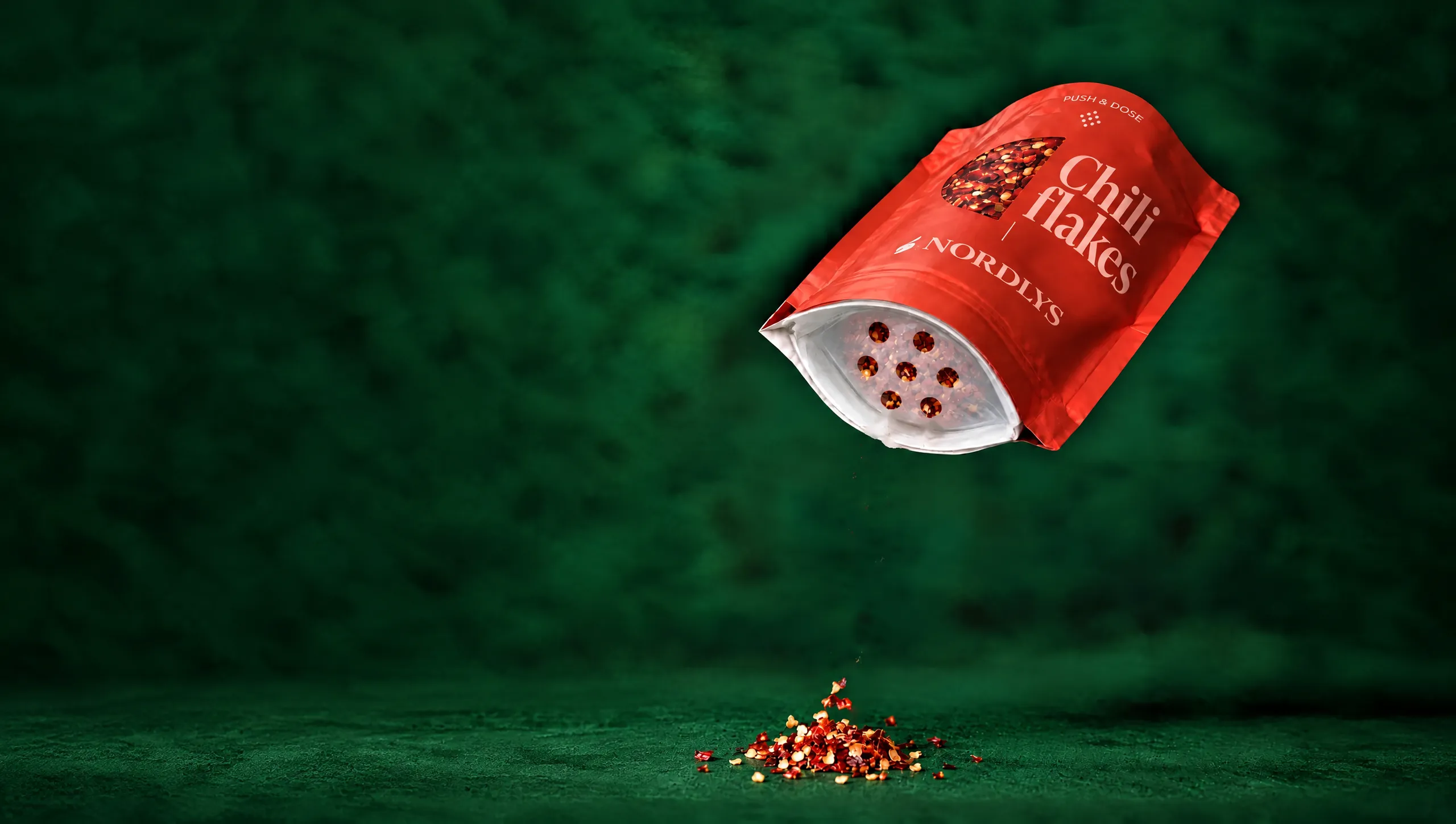 Chili flakes pouch tipped opening-down, chili sprinkling out through the Push&Dose membrane